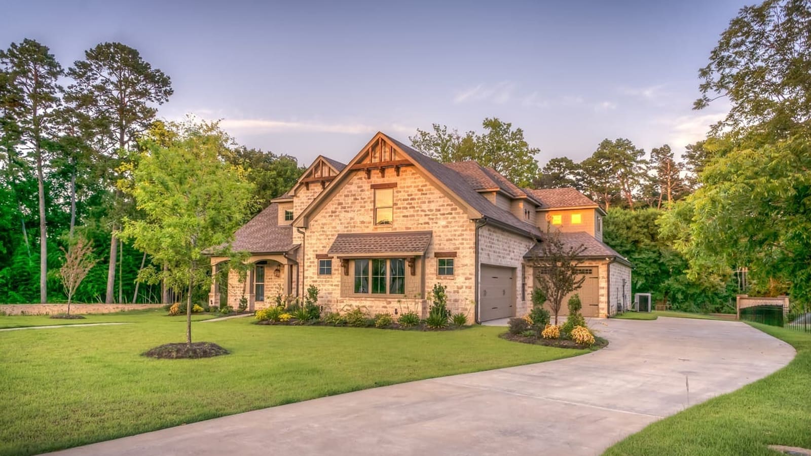 A two-story stone and brick house with a green lawn and a wide concrete driveway on a clear day
